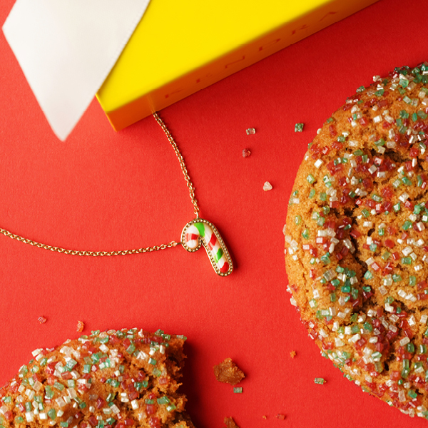 red green and white mini candy cane pendant necklace on red surface with gingerbread cookies
